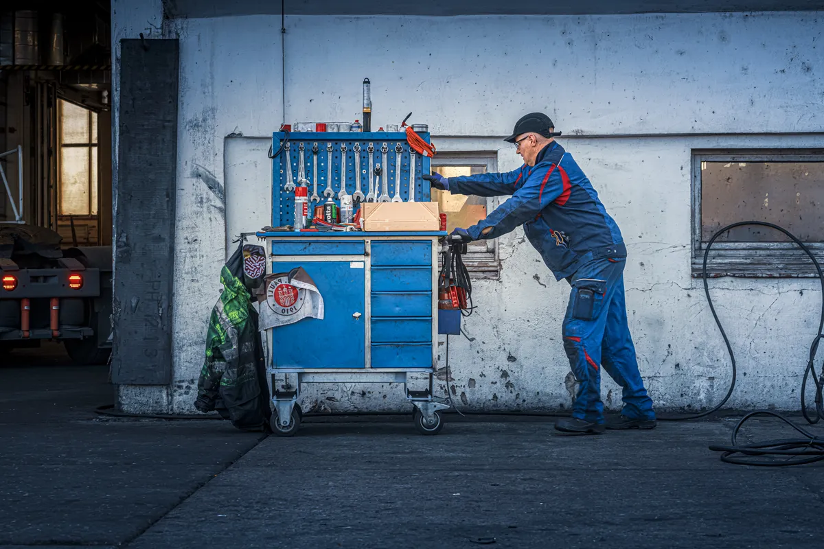 Mechaniker in blauem Overall an einem Werkzeugwagen vor einer Werkstattwand