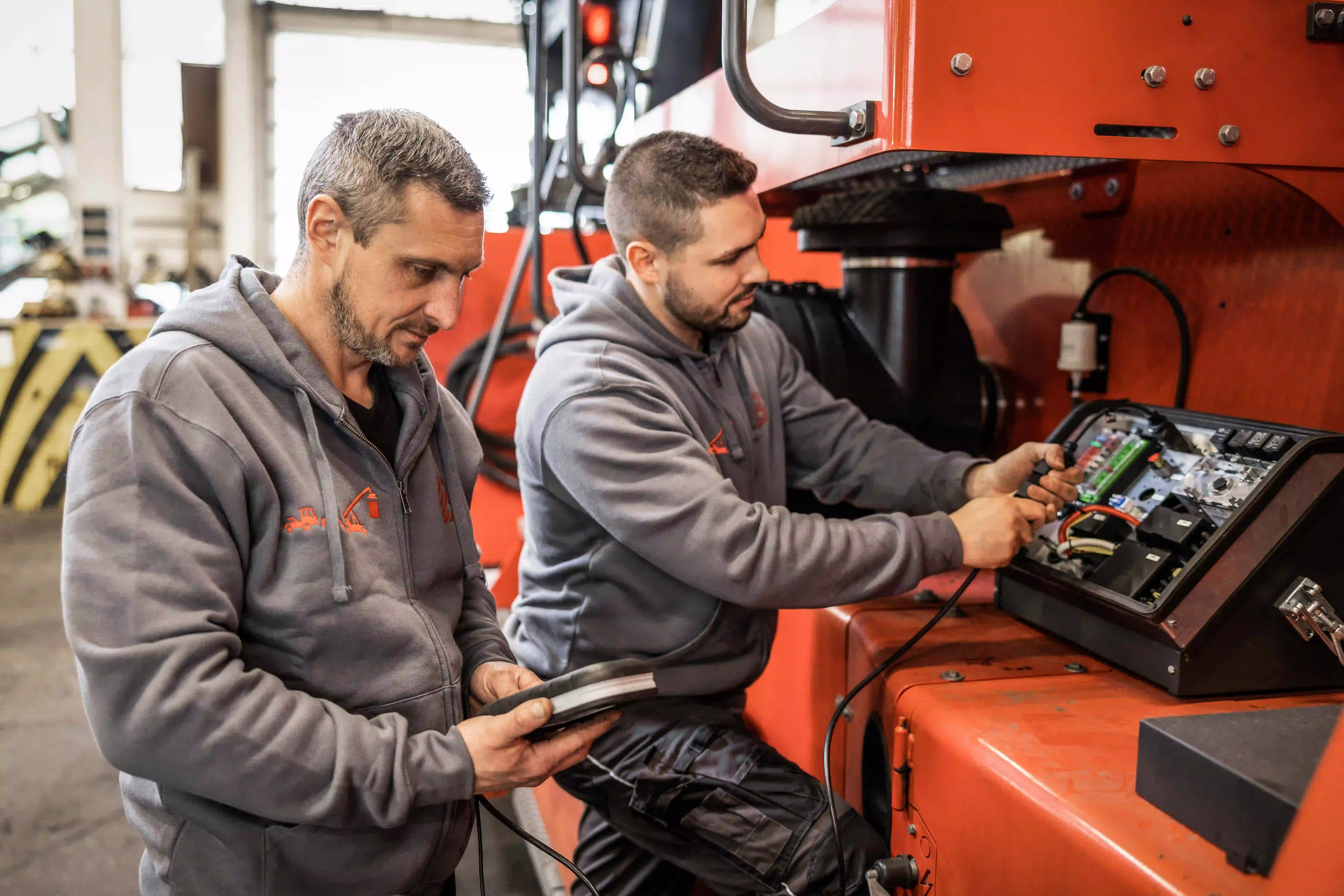 Zwei Mechaniker arbeiten an der Bedienkonsole einer orangefarbenen Hafenmaschine