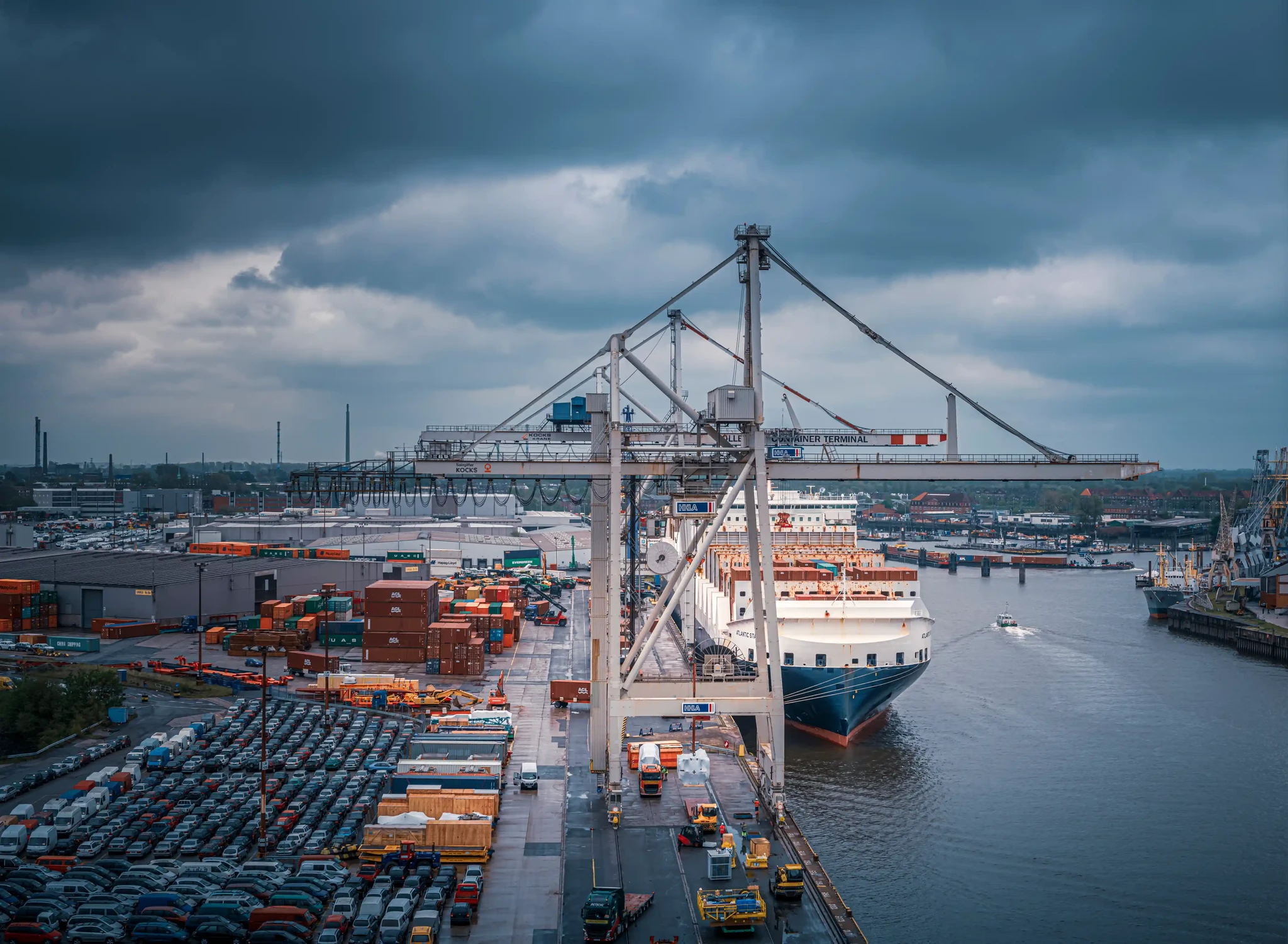 Hafenterminal mit Portalkränen, Schiff am Kai und abgestellten Fahrzeugen