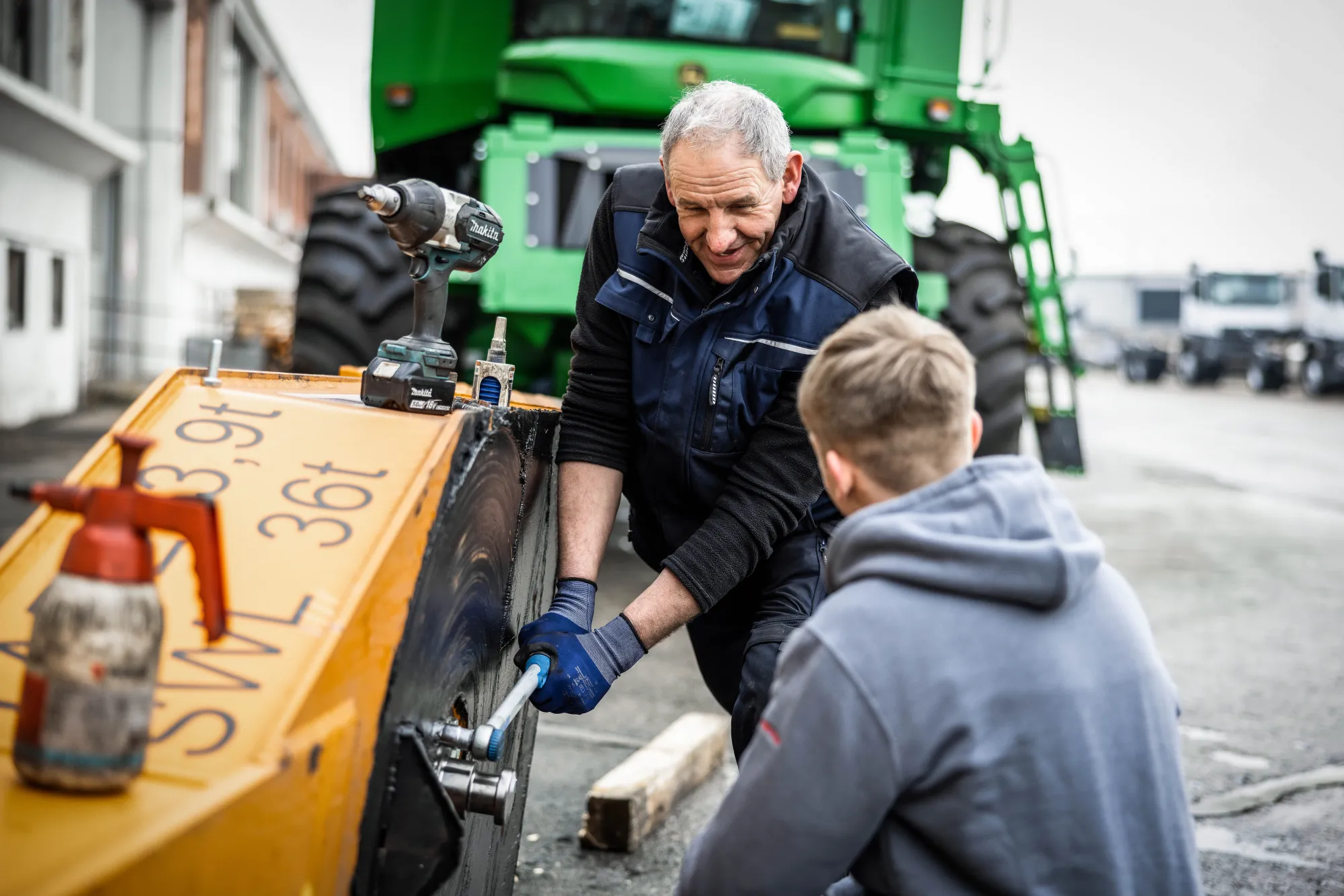 Zwei Mechaniker arbeiten am Rad einer gelben Maschine auf dem Werkstatthof