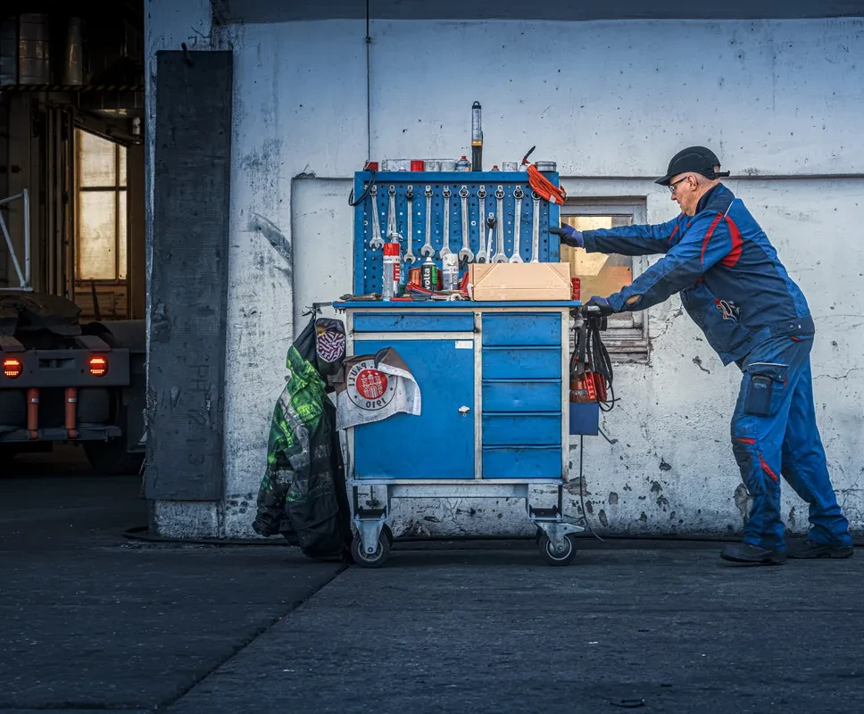 Mecánico con mono azul junto a un carro de herramientas delante de la pared de un taller