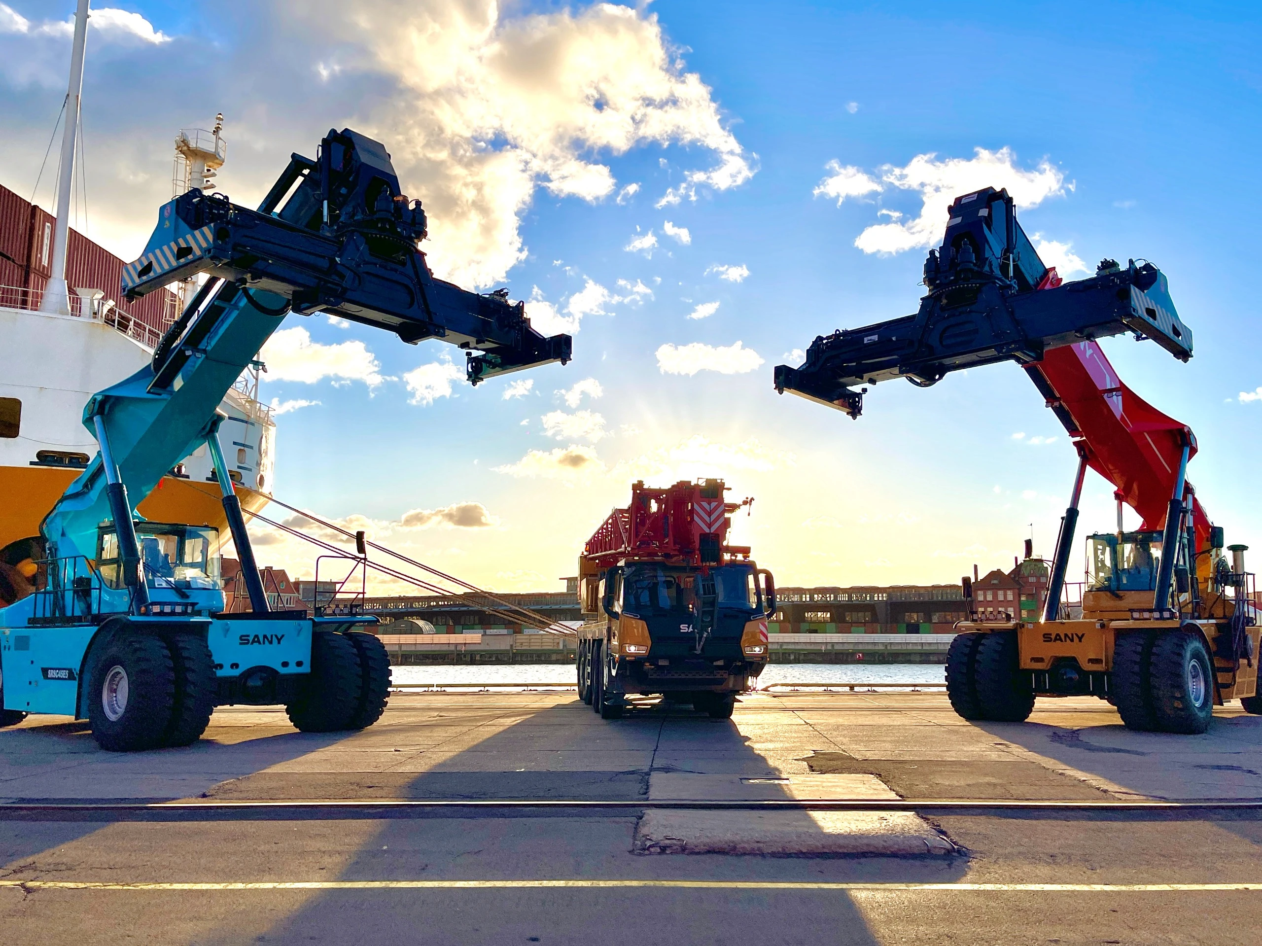Mehrere Reachstacker mit angehobenen Auslegern am Hafenkai im Abendlicht
